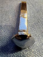 Top view of the shiny chrome railroad spike showing flat, rounded head and some surface wear.