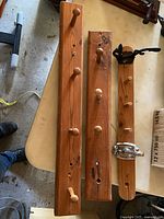 Photo showing three hand made wooden coat holders placed on table. Each has multiple wooden knobs for hanging.