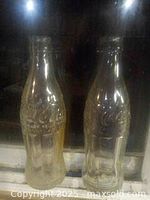 Photo of two clear, heavy antique Coca-Cola glass bottles with embossed logos standing side by side.