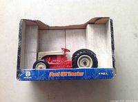 Clear view of the Ford 8N die cast metal tractor in original box, showing the tractor's red and gray colors and black tires inside a blue branded box.