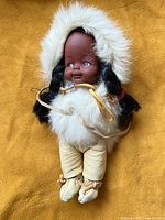 Front view of vintage doll with dark brown face, black hair, and original leather and fur outfit.