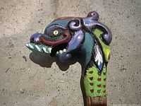 Close-up of the hand carved and hand painted dragon head handle on the wooden walking cane, showing detailed colorful paint and carving.