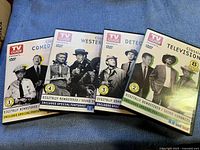 Four classic TV Guide DVDs laid out on a blue fabric surface, showing cover titles Comedy, Western, Detective, and Classic Television.