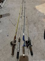 Four fishing rods with reels laid on the floor showing full length and handles