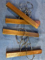 Four vintage wooden pant hangers with metal clips and hooks, laid on a gray fabric surface.