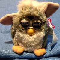 Front view of Furby showing brown-eyed character with orange beak and feet, tan and white fur.