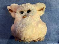 Top view of a fluffy plush Furby with beige beak, furry ears and large eyes.