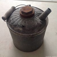 Photo of vintage galvanized metal gas can showing lid, handle, and spout, with wear and rust evident on lid and handle.