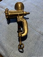 Side view of vintage metal meat grinder with clamp clamp fully visible showing 'SEKONATOR' text embossed on side.