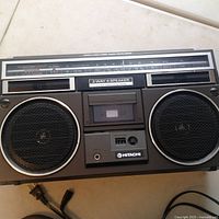 Front view of Hitachi boom box showing speakers, cassette player with headphone jack, and radio tuner dial.
