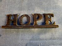 Front view of the metal painted HOPE sign showing block letters on a horizontal base with surface wear.