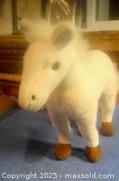 Photo showing front and side view of the white plush horse toy on a fabric surface near a window.