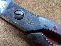 Close-up photo of metal scissors showing red paint on handles and brand engraving 'Alvin' on the side.