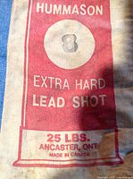 Close up of a canvas bag label reading 'Hummason Extra Hard Lead Shot, size 8, 25 lbs, Ancaster, Ontario, Made in Canada'