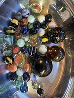Top-down view of multiple glass marbles in a container showing diverse colors, sizes, and patterns.