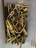 Container filled with assorted used metal hardware including screws, bolts, washers, nuts, anchors, and hooks in various sizes and finishes.