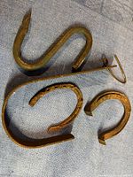 Photo of four metal items on fabric surface: two horseshoes and two bent metal hooks, showing rust and wear.