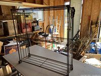 Black metal shelving unit with three wire shelves in a garage or storage area, showing its structure and condition.