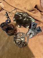 Photo showing shell-shaped metal dish, cowboy boots sculptures, floral trivet, and napkin rings on stand