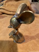 Photo showing a solid brass mouse figurine with large ears and a standing pose on a soft background.