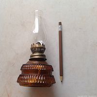 Full view of amber glass oil lamp with textured honeycomb base, brass burner, and clear glass chimney next to a pencil for scale.