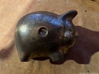 Side view of a solid brass piggy bank showing the rounded shape, pig features, and a keyhole or coin removal slot.
