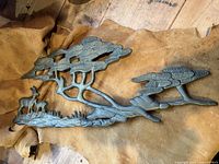 Old brass wall hanging showing a side view of a brass deer and trees landscape piece resting on brown leather or hide