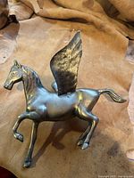 Angled front-left view of the brass Pegasus sculpture showing details of the head, front legs, and raised wing.