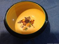 Top view of the ceramic fruit bowl showing the painted fruit decoration inside, set on a textured blue fabric.