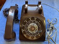 Top view of vintage brown rotary dial telephone showing dial with numbers and letters, handset, and cords.