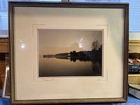 Full view of the framed black and white photo showing a calm lake with reflections of trees and a horizon at sunset or sunrise.