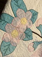 Close-up of pink flower and blue-green leaf appliques stitched on cream fabric