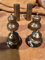 Front view of all three pairs of old brass salt and pepper shakers grouped in two rows, showing detailed tops and enamel decoration on one pair