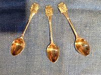 Front view of three shamrock-topped silver plated sugar spoons laid side by side on a blue textured surface.