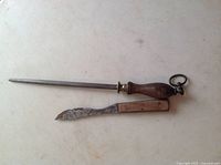 Knife and honing steel sharpener laid flat on a white surface, showing wooden handles and worn blade on the knife.