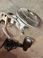 Photo showing two clip-on devices: a white circular fan and a brown spotlight lamp lying on the floor.