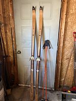 Full view of downhill skis and ski poles standing against a door showing the full height and design of the skis and poles.