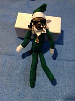 Photo of a 6-inch Snoop Dogg doll wearing a green elf outfit with white trim hat, sunglasses, gold chain with marijuana leaf pendant, and a cigar.