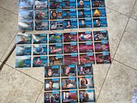 Photo of 39 Star Trek collector cards in protective sleeves, laid out on the floor. Cards depict characters, starships, and logos from the franchise.