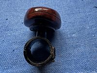 Close-up photo of the steering wheel handle showing the woodgrain knob and metal clamp for attachment.