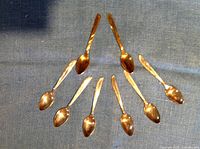 Top view of all eight spoons arranged in a semicircle showing six silver plated and two copper spoons.