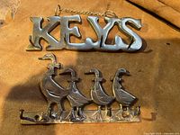 Photo showing two brass key holders; one with the word 'KEYS' and the other shaped as four ducks.
