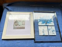 Two picture frames side by side on a blue cloth; left is white with photo placeholder, right is clear glass with blue flower placeholders
