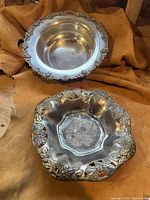 Two silver plated bowls viewed from the top showing decorative rims and floral patterns.