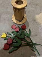 Photo showing swivel wooden utensil holder with round base and several holes for placing wooden tulips on top of pegs, set on concrete floor.