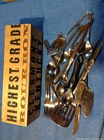 Wooden box filled with various metal utensils including forks, spoons, slotted spatula, butter knife, fish spatula, and others.