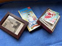 Framed black and white photo, Frosty the Snowman VHS tape box, and Christmas cards box on blue fabric