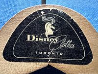 Close-up photo of the top center part of the wooden hanger highlighting the black Disney Clothes Toronto logo with an embossed horned animal head and cursive text.