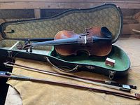 Open violin case showing violin, bow, and rosin box inside, all laid out on a wooden surface.