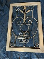 Rectangular wall plant holder with light wood frame and metal scrollwork with leaves laid flat on blue tarp